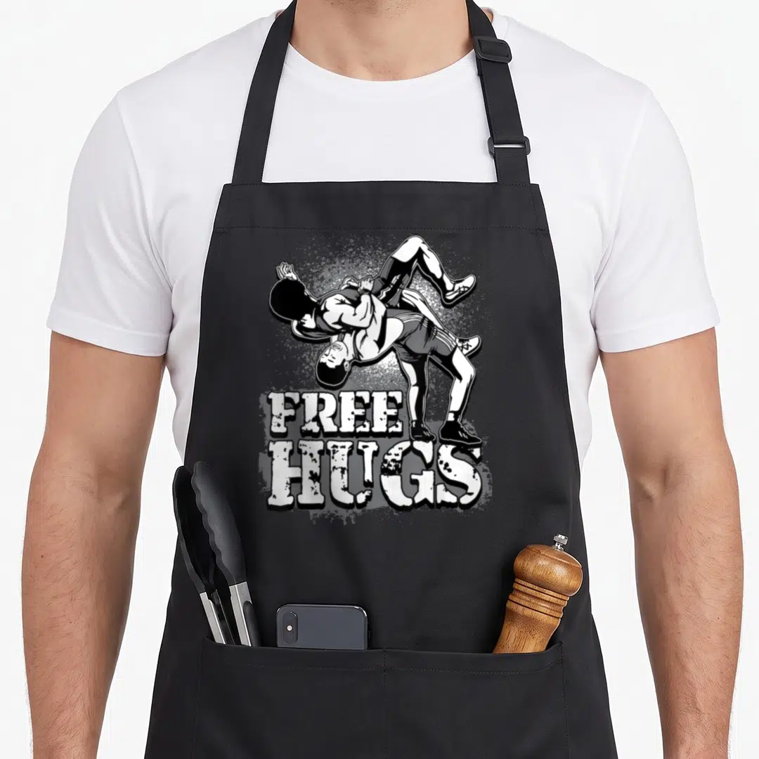 Crush wrestling apron - Two wrestlers grappling above white distressed text reading FREE HUGS in black and white — shown on a black cotton canvas apron against a white background