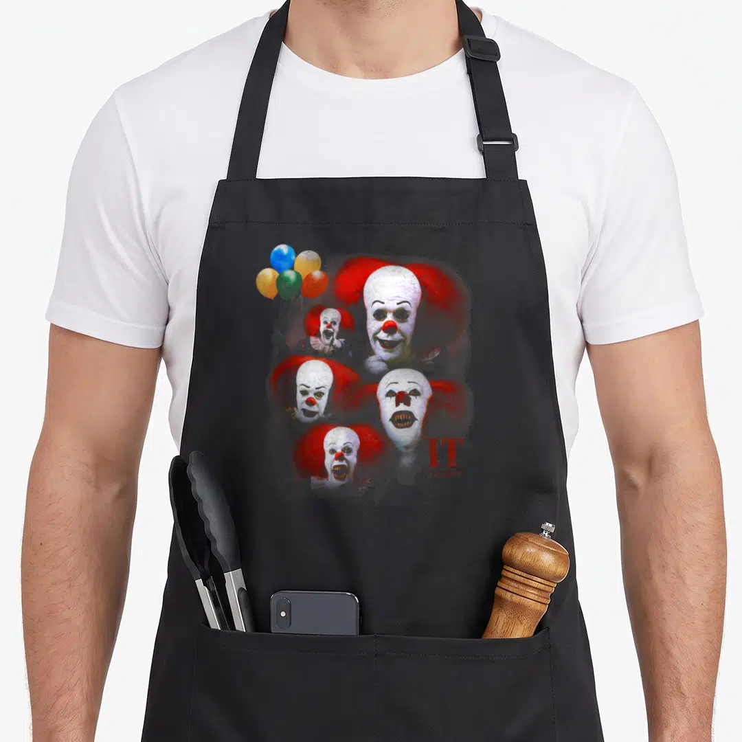 Funny many face apron - Five Pennywise heads with balloons and IT THE MOVIE text — shown on a black cotton canvas apron against a white background
