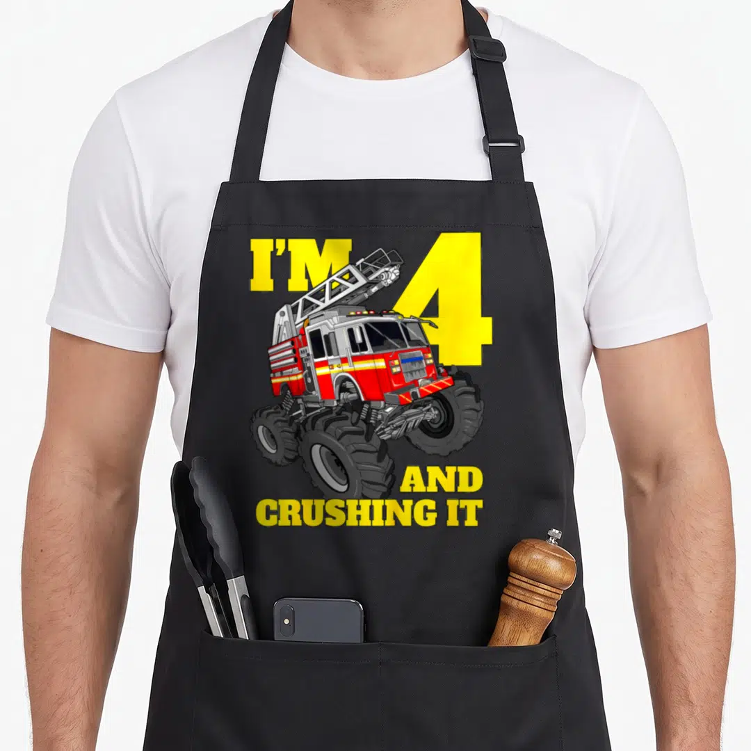Four firefighter truck apron - Cartoon monster fire truck over yellow number 4 with text I'M 4 AND CRUSHING IT — shown on a black cotton canvas apron against a white background