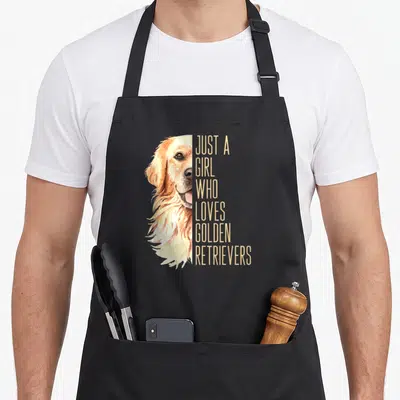 Enthusiast golden retriever apron - Watercolor golden retriever head next to stacked text reading just a girl who loves — shown on a black cotton canvas apron against a white background