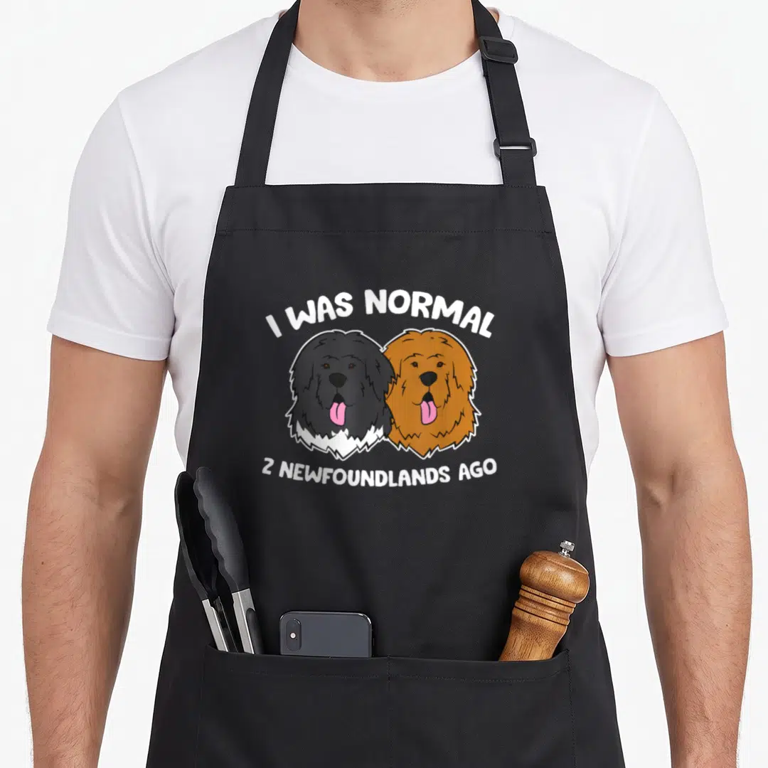 Ich dog apron - Two cartoon Newfoundland heads in black and brown with pink tongues under white text — shown on a black cotton canvas apron against a white background
