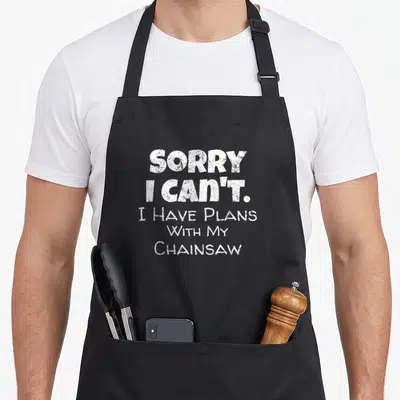 Lumberjack service apron - White distressed text reading Sorry I Can't I Have Plans With My Chainsaw — shown on a black cotton canvas apron against a white background
