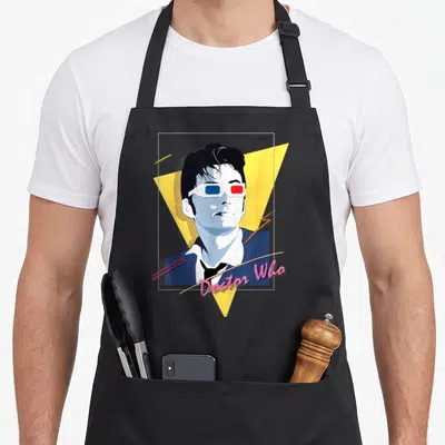 Tenant 80s apron - Retro man in 3D glasses over yellow triangle with pink Doctor Who script text — shown on a black cotton canvas apron against a white background