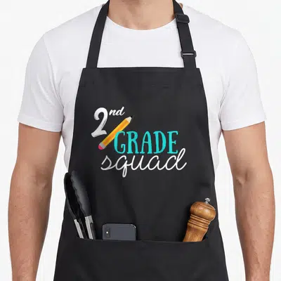Teacher second 2nd apron - 2nd GRADE squad text with diagonal pencil in white cyan and yellow — shown on a black cotton canvas apron against a white background