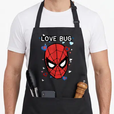 Bug valentine's day apron - LOVE BUG text above Spider-Man mask with hearts and small spiders in red blue white black — shown on a black cotton canvas apron against a white background