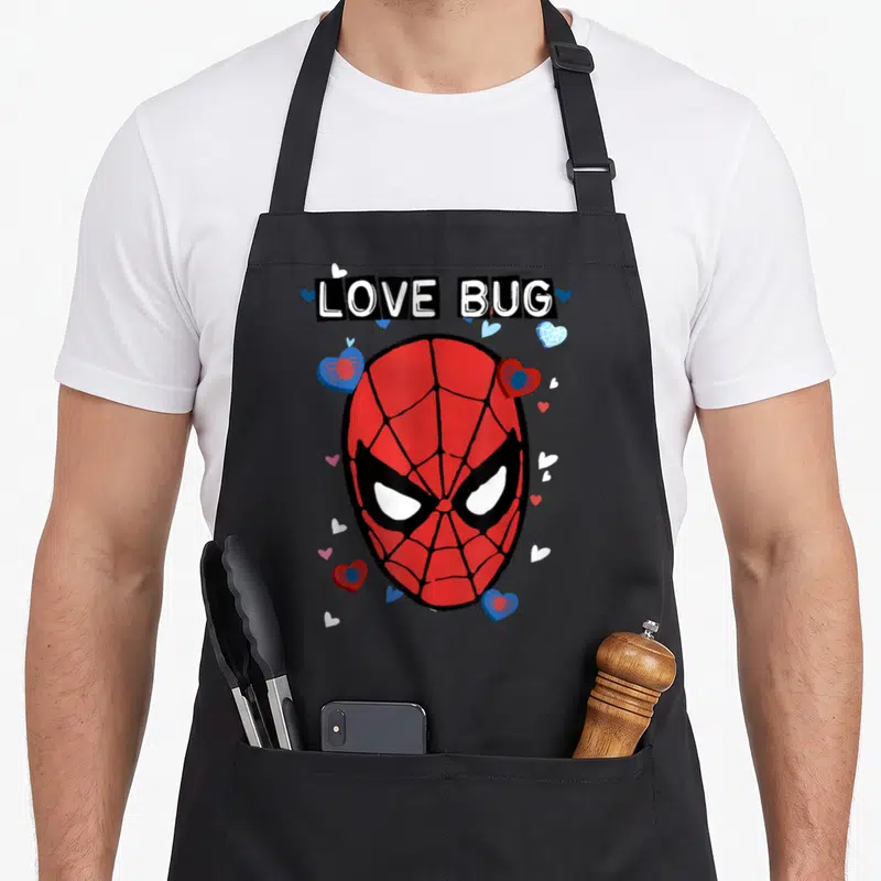 Bug valentine's day apron - LOVE BUG text above Spider-Man mask with hearts and small spiders in red blue white black — shown on a black cotton canvas apron against a white background
