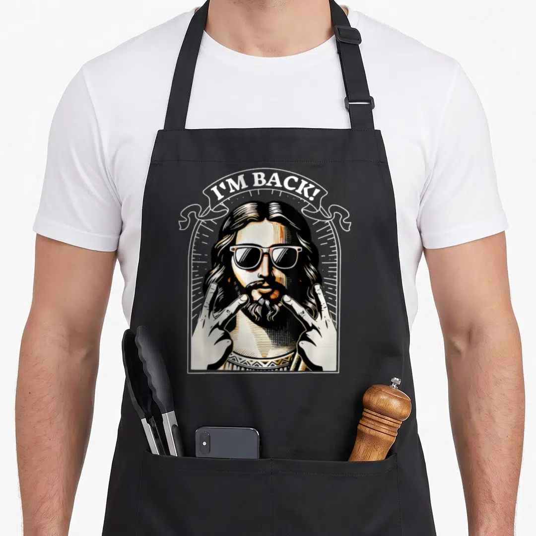 Jesus sunglass easter apron - Cartoon Jesus with sunglasses and double peace signs under I'M BACK banner — shown on a black cotton canvas apron against a white background