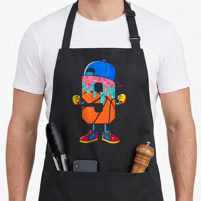 Youth 9th ice cream apron - Orange basketball character with blue cap, pink and blue frosting drip, and colorful — shown on a black cotton canvas apron against a white background