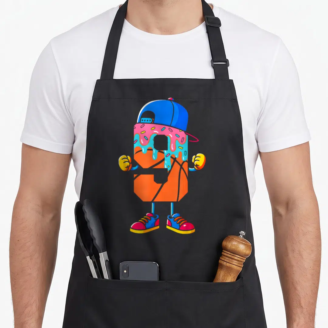 Youth 9th ice cream apron - Orange basketball character with blue cap, pink and blue frosting drip, and colorful — shown on a black cotton canvas apron against a white background