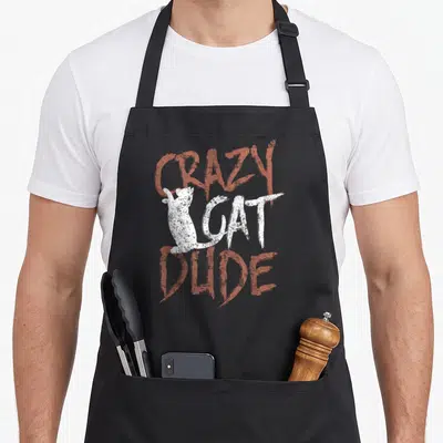 Dude black cat aprons - Distressed red and white text reading CRAZY CAT DUDE with white cat silhouette — shown on a black cotton canvas apron against a white background