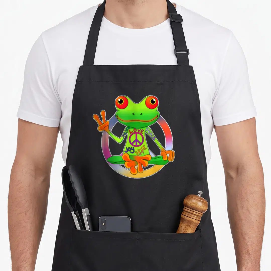 Hippie frog aprons - Green frog in lotus pose making peace sign with rainbow circle and text Faith Love Peace Joy Hope — shown on a black cotton canvas apron against a white background