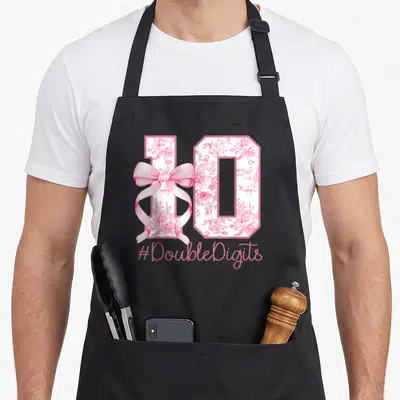 10th bow apron - Number 10 filled with pink roses and a ribbon bow with hashtag text — shown on a black cotton canvas apron against a white background