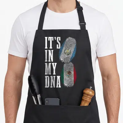Guatemala mexico apron - IT'S IN MY DNA text next to two fingerprints filled with Guatemalan and Mexican flag colors — shown on a black cotton canvas apron against a white background