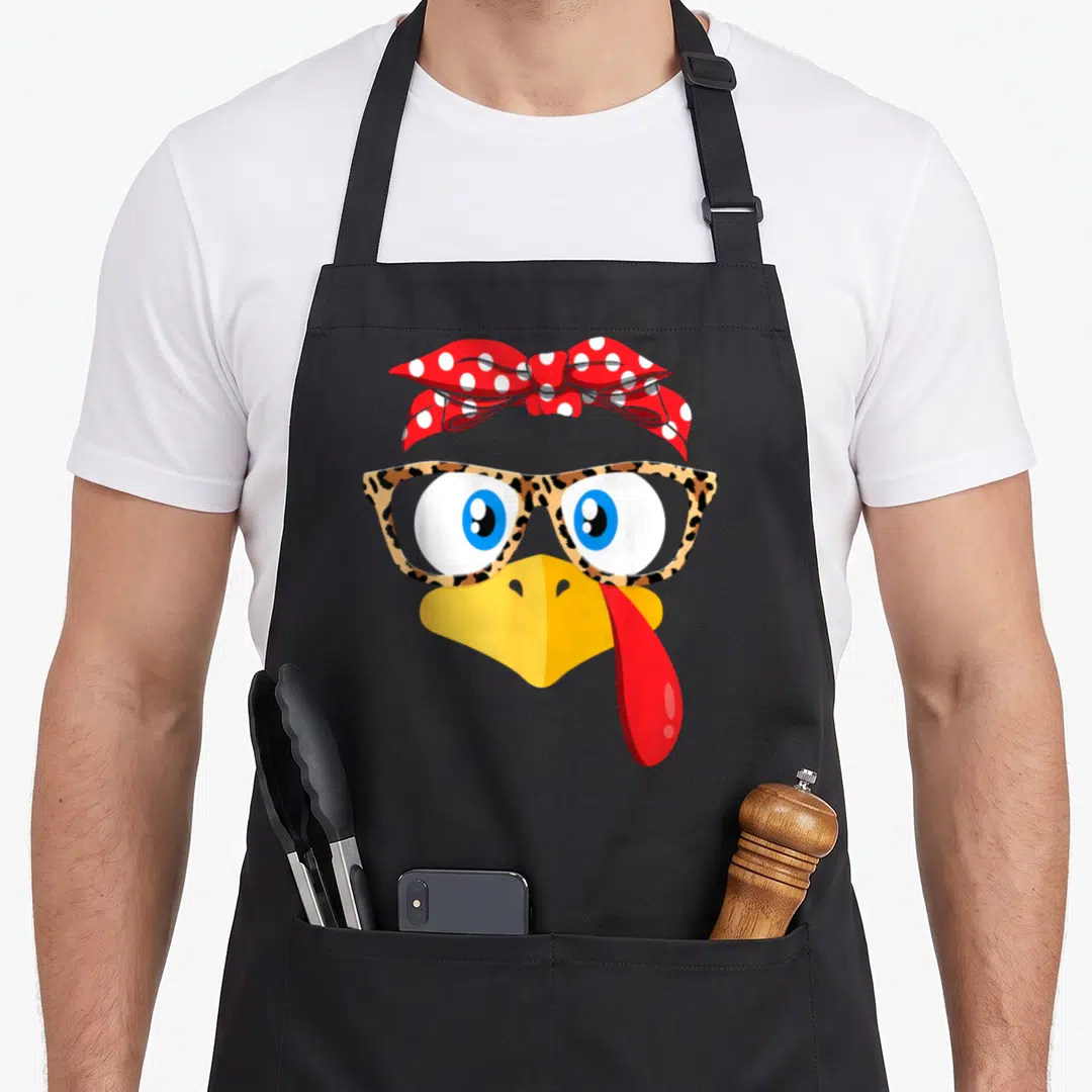 Glass thanksgiving apron - Cartoon chicken face with leopard glasses and red polka dot bandana — shown on a black cotton canvas apron against a white background