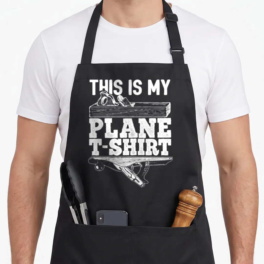 Plane carpenter woodworking apron - White distressed text reading THIS IS MY PLANE T-SHIRT with hand plane illustrations — shown on a black cotton canvas apron against a white background