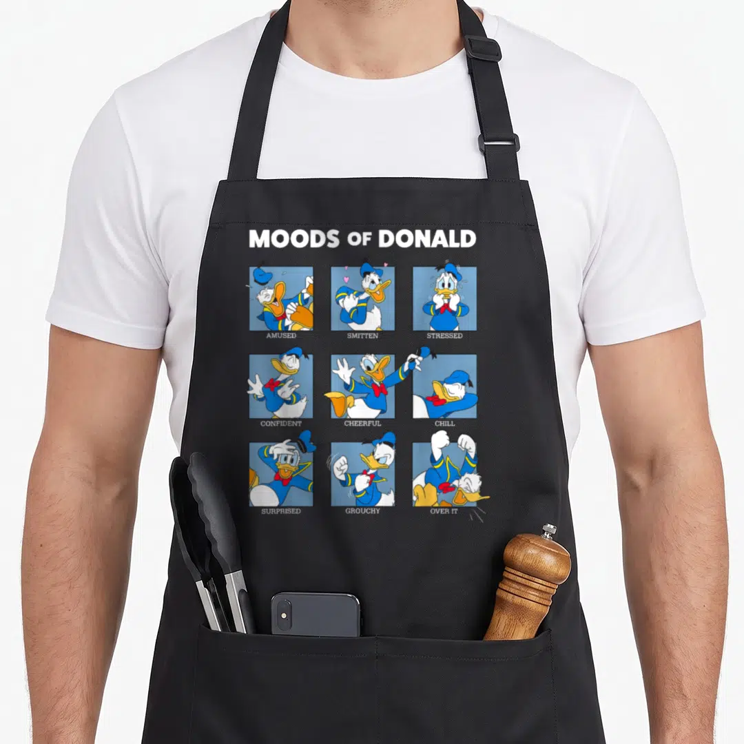 Friend duck apron - Moods of Donald cartoon grid with Amused Smitten Stressed Confident Cheerful Chill Surprised — shown on a black cotton canvas apron against a white background