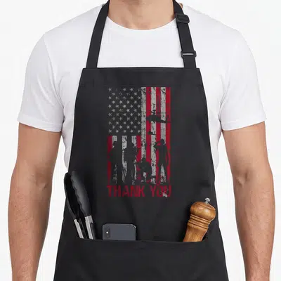 Memorial american flag apron - Distressed red and grey flag with soldier silhouettes and THANK YOU text — shown on a black cotton canvas apron against a white background
