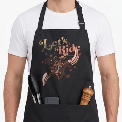 Ride camping apron - Retro Let's Ride text above Woody and Jessie on horse with rainbow and stars — shown on a black cotton canvas apron against a white background