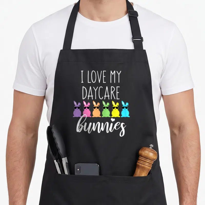 Easter daycare teacher aprons - Six colorful cartoon bunnies wearing sunglasses below stacked white text reading I Love — shown on a black cotton canvas apron against a white background