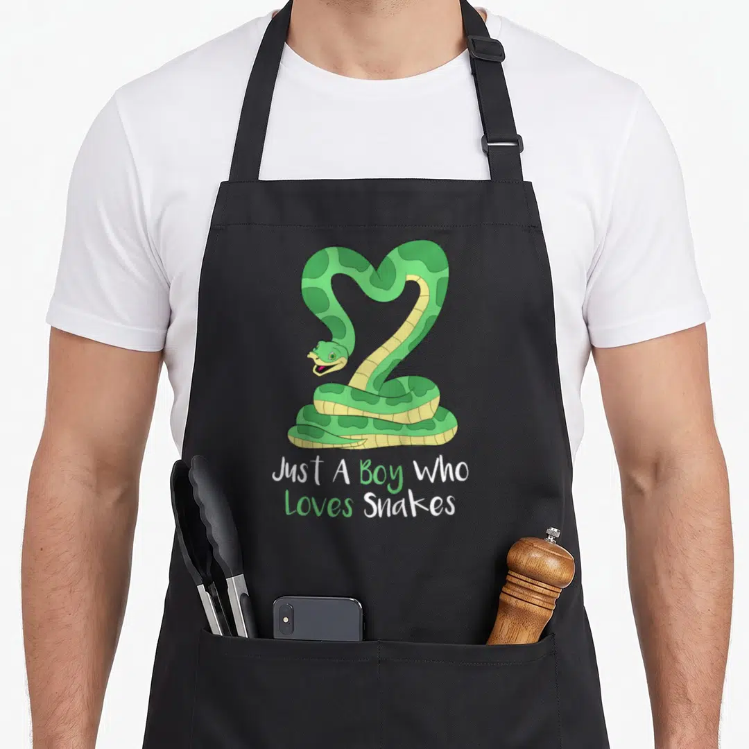 Snake boa apron - Cartoon green snake coiled above white and green text reading Just A Boy Who Loves Snakes — shown on a black cotton canvas apron against a white background