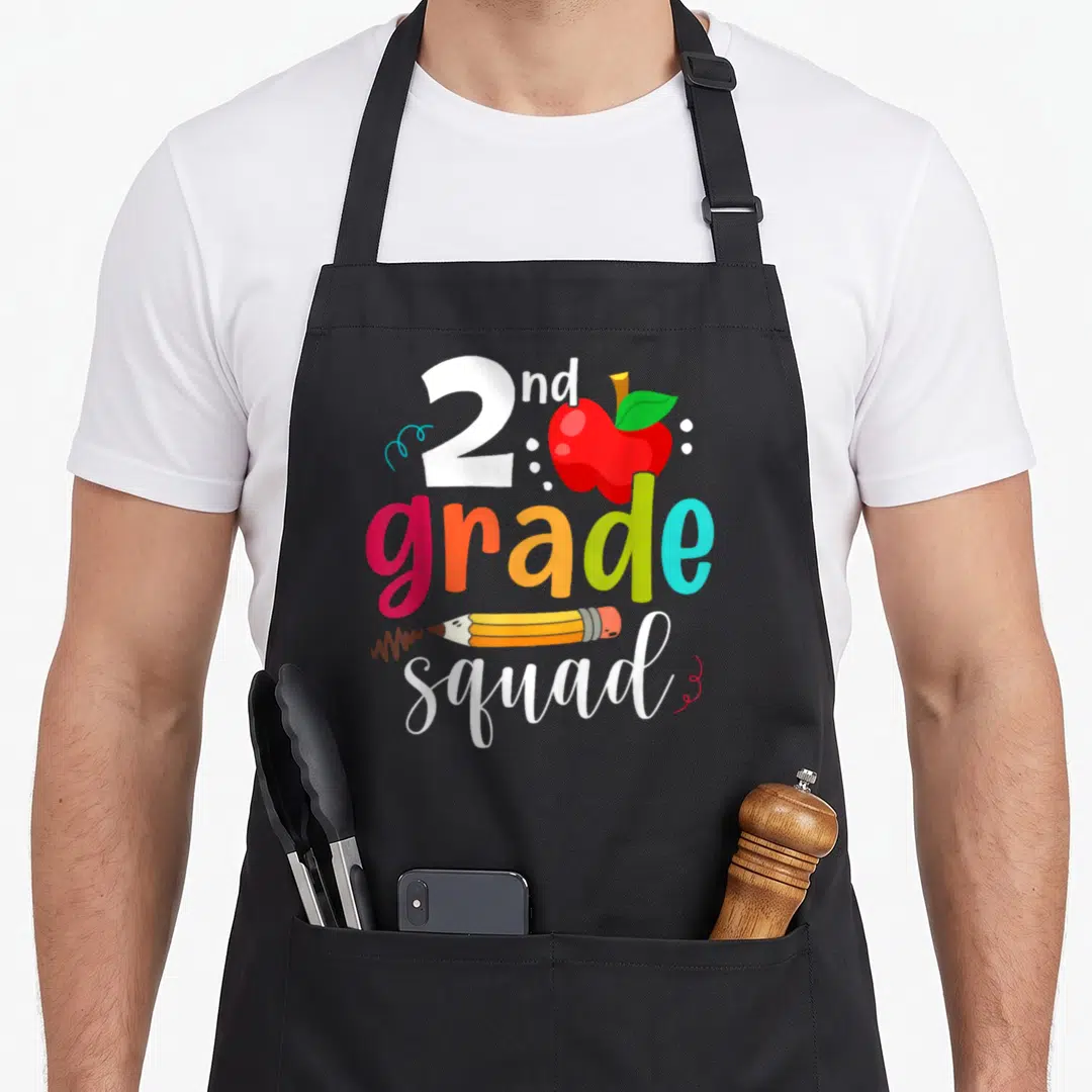 Squad school 2nd apron - Red apple, yellow pencil, and multi-colored 2nd grade squad text on black background — shown on a black cotton canvas apron against a white background