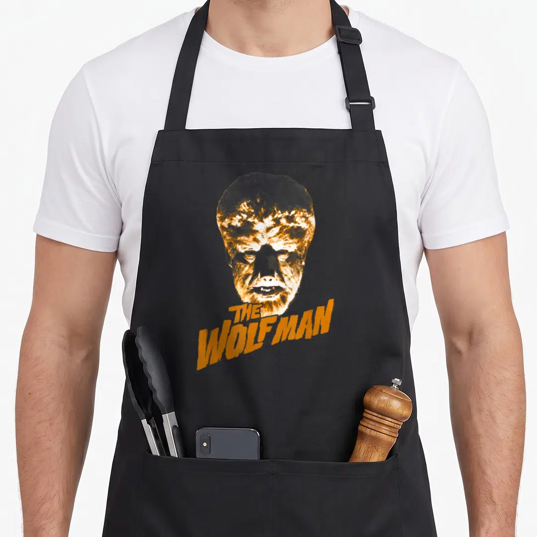 Wolf universal monsters apron - Distressed orange and white wolfman head above THE WOLFMAN text on black fabric — shown on a black cotton canvas apron against a white background