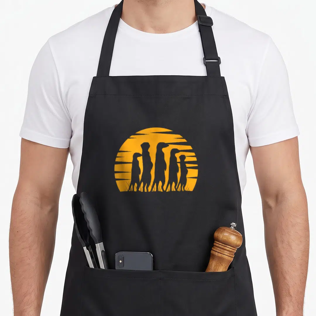 Fan animal apron - Five grey meerkat silhouettes standing before an orange sun with horizontal stripes — shown on a black cotton canvas apron against a white background