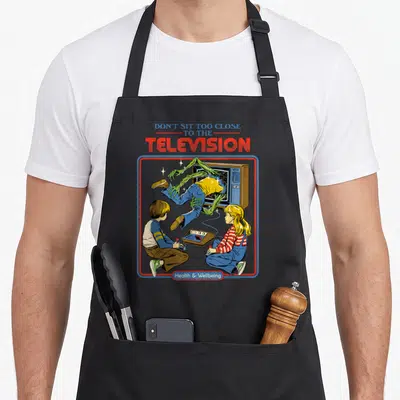 Sit steven rhodes apron - Red and blue frame around green monster pulling person into TV, text Don't Sit Too Close — shown on a black cotton canvas apron against a white background