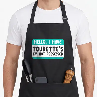 Disorder ribbon apron - Teal and grey name tag graphic reading Hello I Have Tourette's I'm Not Possessed — shown on a black cotton canvas apron against a white background