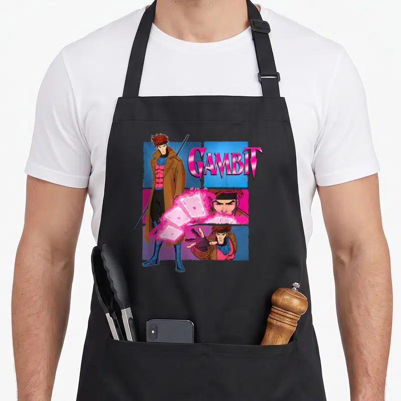 Studio x apron - Gambit cartoon figure with pink blue brown panels and glowing cards — shown on a black cotton canvas apron against a white background