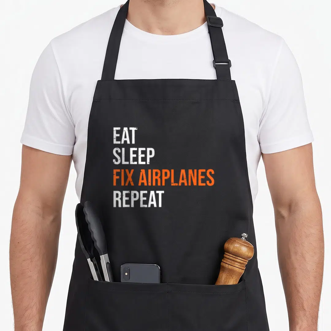 Mechanic aircraft apron - Stacked white and orange text reading EAT SLEEP FIX AIRPLANES REPEAT — shown on a black cotton canvas apron against a white background