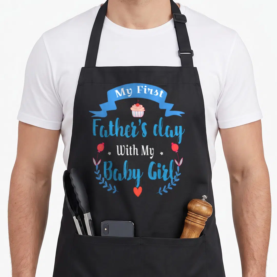 1st baby father day apron - Blue ribbon My First Father's day With My Baby Girl cupcake and heart design — shown on a black cotton canvas apron against a white background