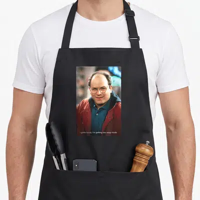 George 90s apron - Photo of man in red jacket and blue shirt with text I gotta focus I'm getting into soup mode — shown on a black cotton canvas apron against a white background
