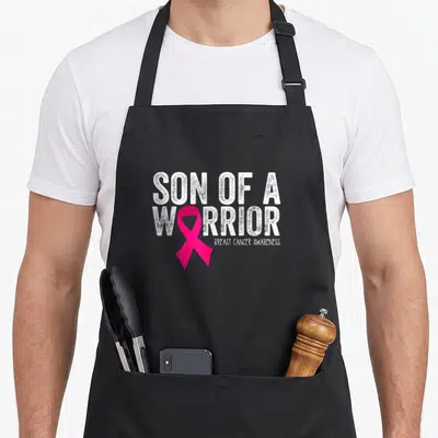 Son breast cancer awareness aprons - Distressed white Son of a Warrior text with pink ribbon replacing the O — shown on a black cotton canvas apron against a white background