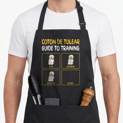 Coton dog training apron - Coton de Tulear training guide with SIT DOWN FETCH and empty STAY box — shown on a black cotton canvas apron against a white background