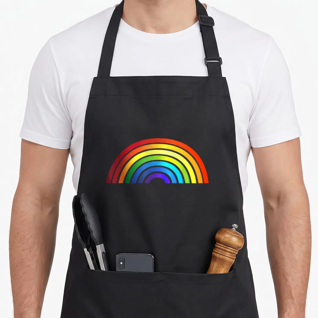 Rainbow stripe apron - Single rainbow arc with red orange yellow green blue purple bands on black background — shown on a black cotton canvas apron against a white background