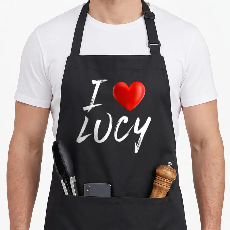 Family i love lucy apron - White I and LUCY text with a red heart symbol — shown on a black cotton canvas apron against a white background