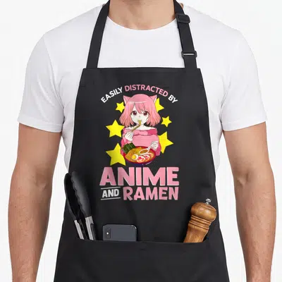 Easily anime apron - Pink haired anime girl eating ramen with stars and text EASILY DISTRACTED BY ANIME AND RAMEN — shown on a black cotton canvas apron against a white background