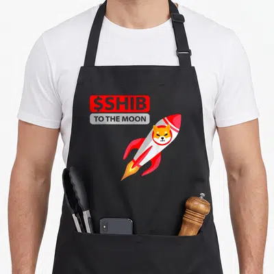 Rocket coin apron - Cartoon rocket with dog face and stacked $SHIB TO THE MOON text in red and grey — shown on a black cotton canvas apron against a white background