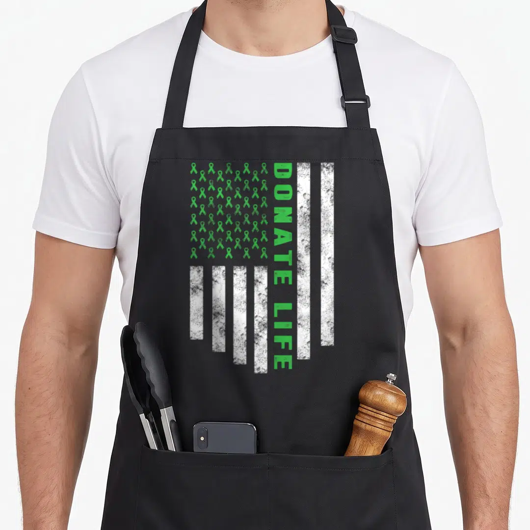 Awareness flag organ apron - Grid of green ribbons next to vertical DONATE LIFE text with distressed white stripes — shown on a black cotton canvas apron against a white background