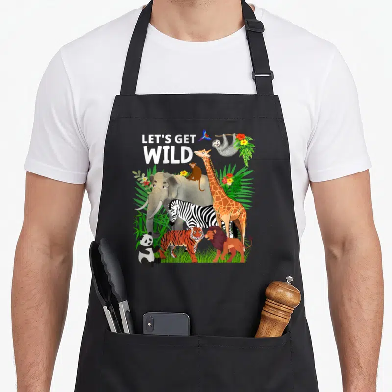 Zoo animal wildlife birthday apron - Cartoon jungle animals with LET'S GET WILD text and tropical leaves — shown on a black cotton canvas apron against a white background