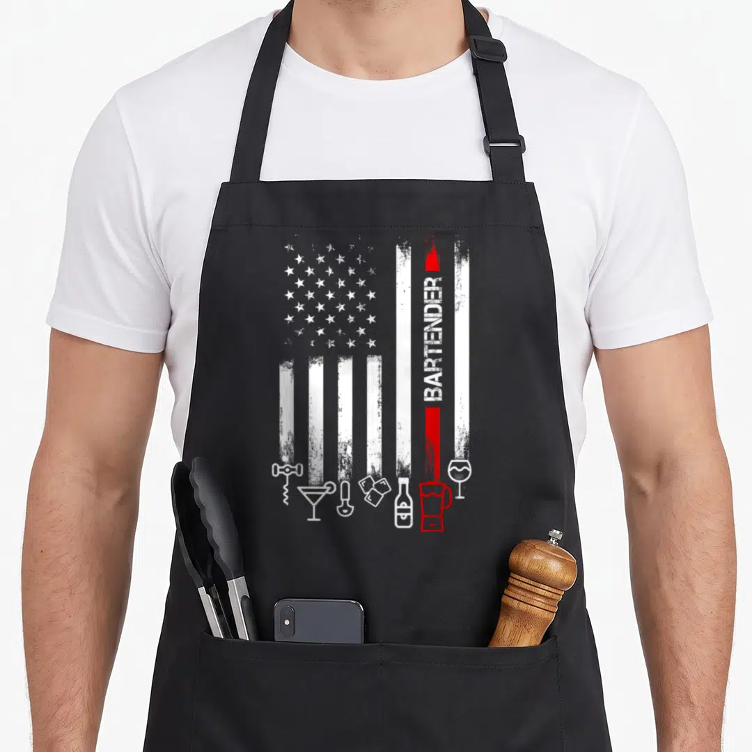 Flag bartender apron - Distressed American flag with vertical BARTENDER text and row of bar tool outlines in white — shown on a black cotton canvas apron against a white background