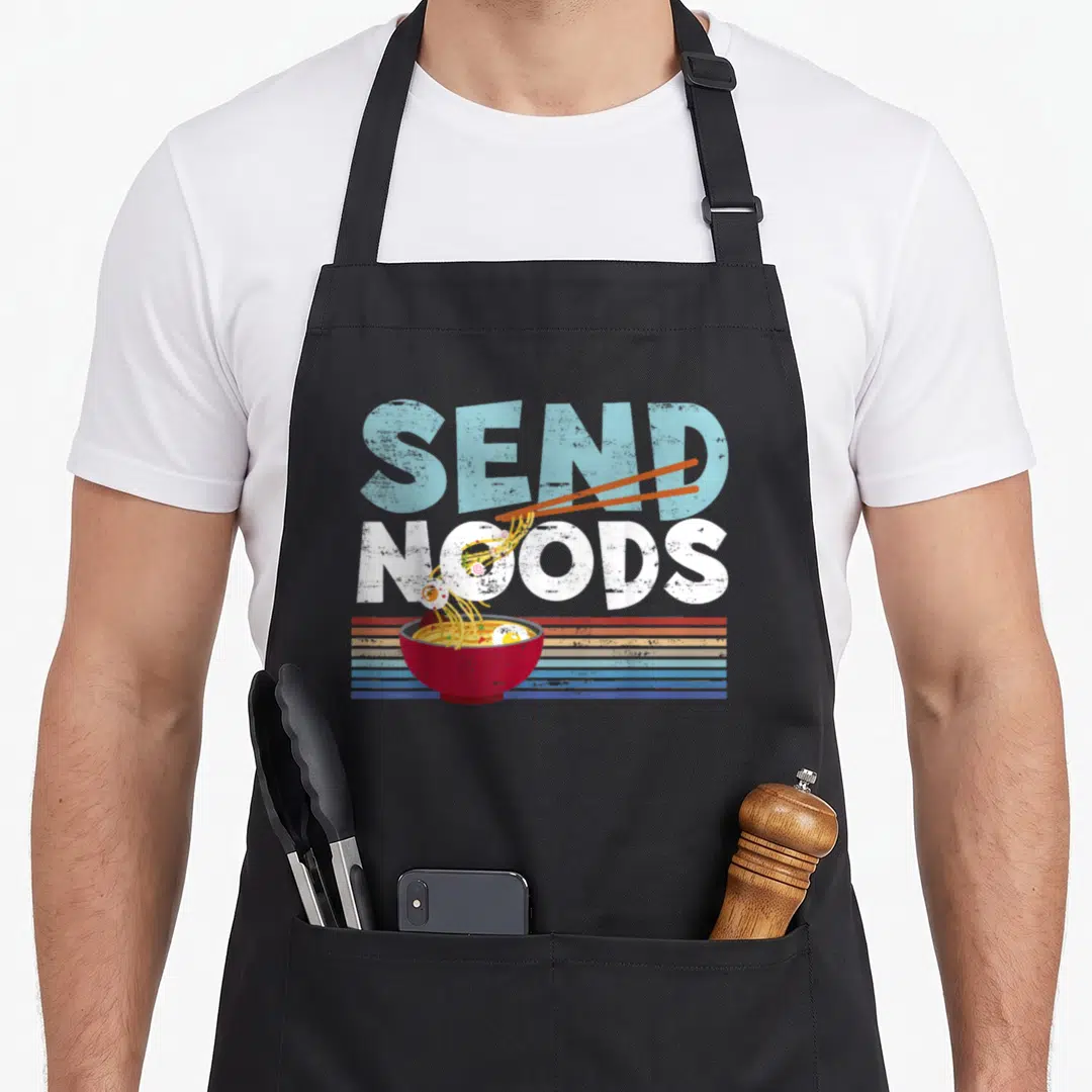 Nood joke apron - Retro graphic of SEND NOODS text with chopsticks lifting noodles from a red bowl against striped — shown on a black cotton canvas apron against a white background