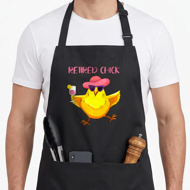 Grandma retirement apron - Cartoon yellow chick with pink hat and purple sunglasses holding cocktail under Retired — shown on a black cotton canvas apron against a white background