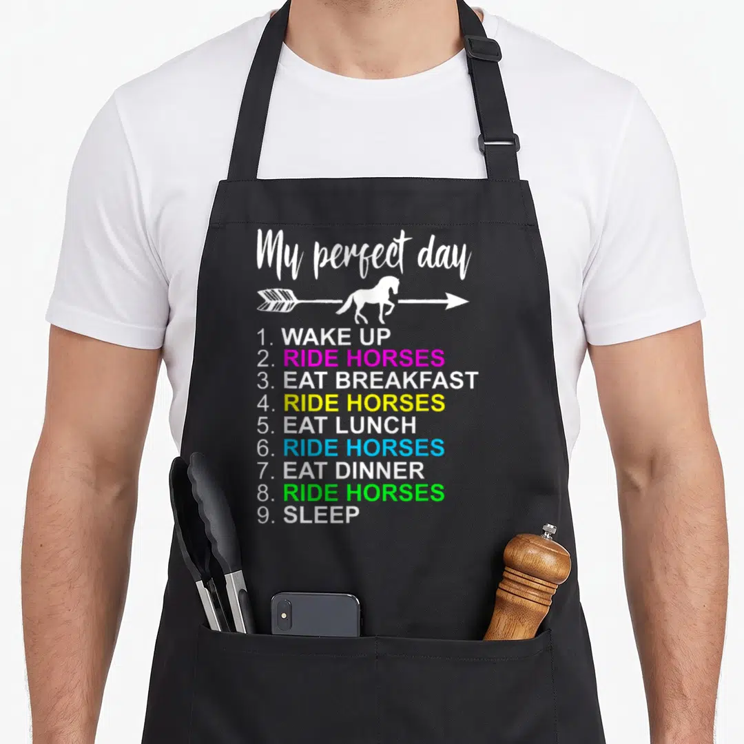Equestrian horse apron for women - My perfect day text with white arrow horse silhouette and colorful numbered list — shown on a black cotton canvas apron against a white background