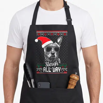 Sleigh dog kitchen apron - Dog in Santa hat and sunglasses with Sleigh ALL DAY text and holiday border — shown on a black cotton canvas apron against a white background