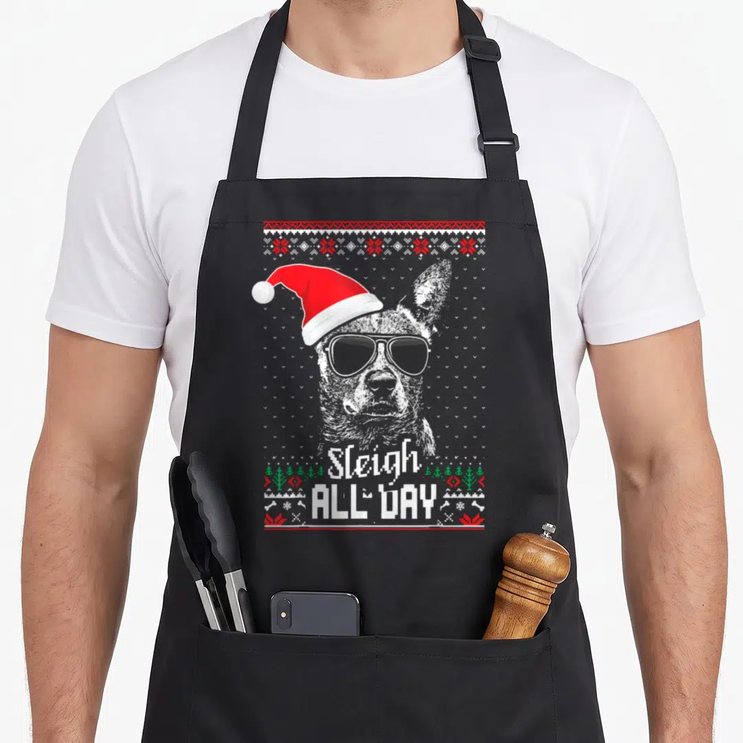 Sleigh dog kitchen apron - Dog in Santa hat and sunglasses with Sleigh ALL DAY text and holiday border — shown on a black cotton canvas apron against a white background