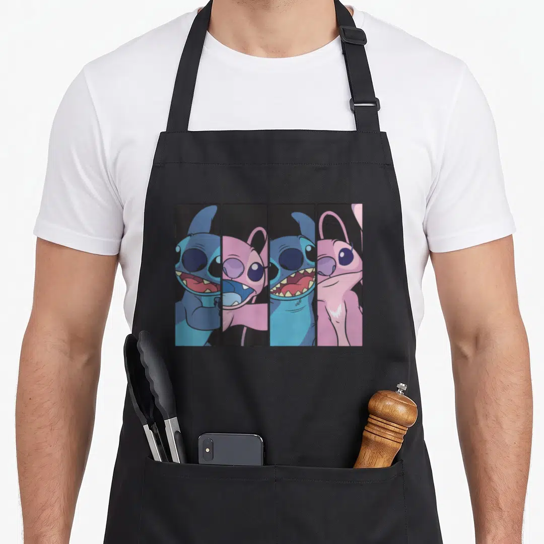 Boxed face apron - Four vertical panels showing blue and pink cartoon characters with large eyes and teeth — shown on a black cotton canvas apron against a white background