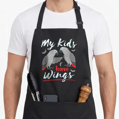African parrot bird apron - Two grey parrots facing each other with red tails and text My Kids have Wings — shown on a black cotton canvas apron against a white background
