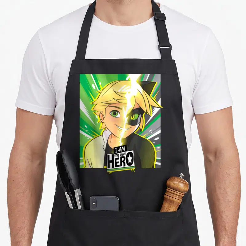 Collection cat apron - Split face cartoon boy with green eyes and black mask under 'I AM my own HERO' text — shown on a black cotton canvas apron against a white background
